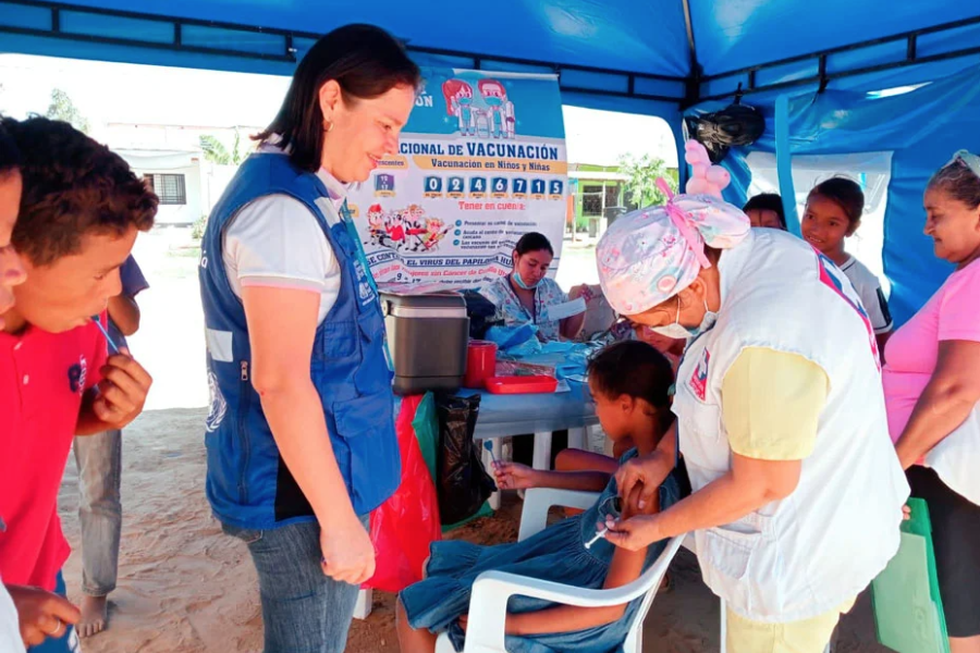 Funcionaria de la OPS/OMS Colombia presente en una carpa de vacunación donde una enfermera está aplicando una vacuna a una niña.