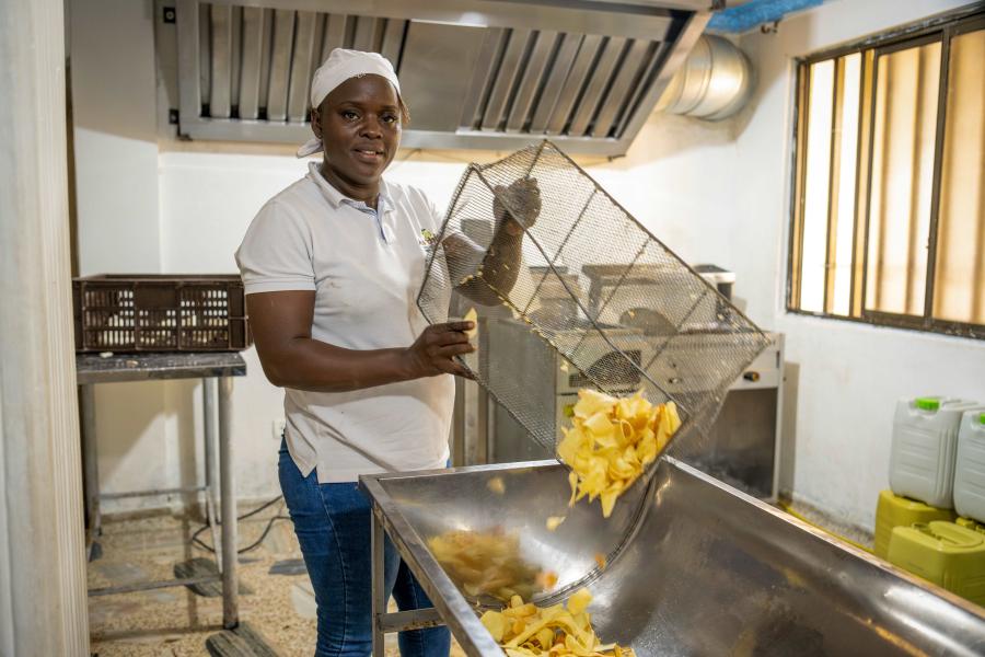 Mujer afrocolombiana en una cocina industrial friendo chips de papachina, mostrando procesos de producción alimentaria artesanal y empoderamiento económico local.