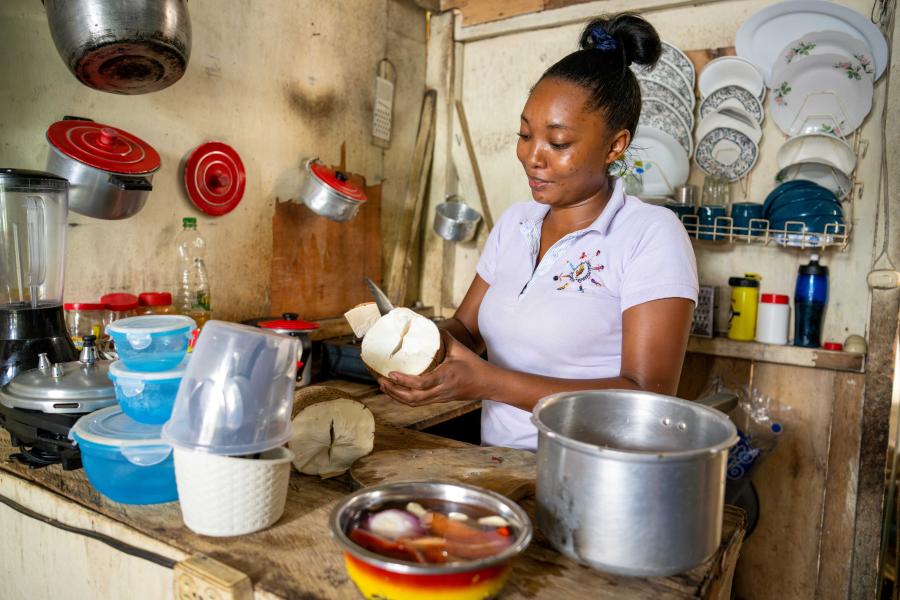 Sorelly, mujer afrocolombiana pelando yuca en una cocina tradicional, rodeada de utensilios y ollas, destacando la preparación de alimentos locales y la vida cotidiana en comunidades rurales.