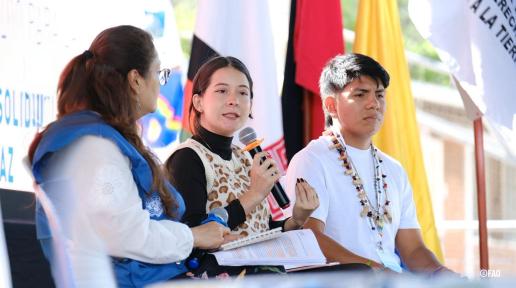 Jóvenes líderes indígenas y representantes de organizaciones internacionales dialogan sobre derechos territoriales y paz en el X Foro Global de la Tierra, con banderas y mensajes de solidaridad de fondo.